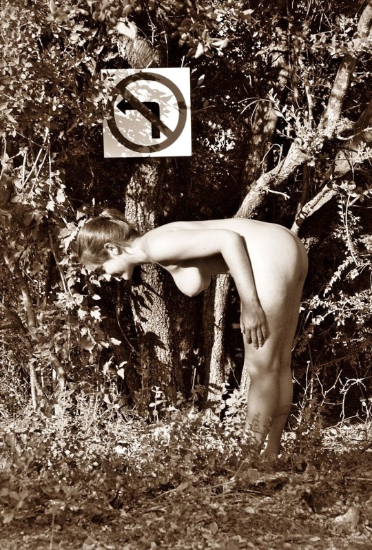 Nude woman bent over near a sign that seems to say "Bending over prohibited"