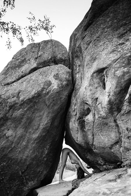 Woman bent over in a triangular space between two rocks