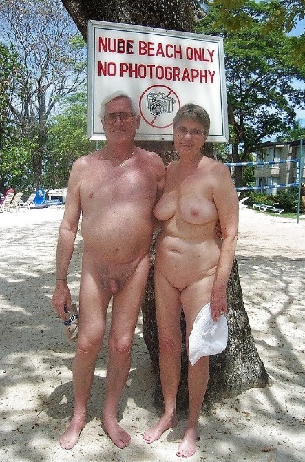 Nudists being photographed near a sign saying 'no photography'